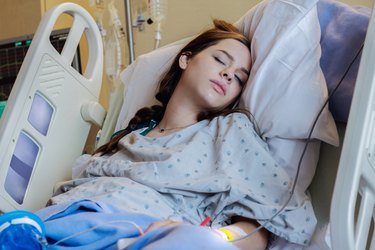 a young adult with long brown hair wearing a hospital gown and sleeping in a hospital bed